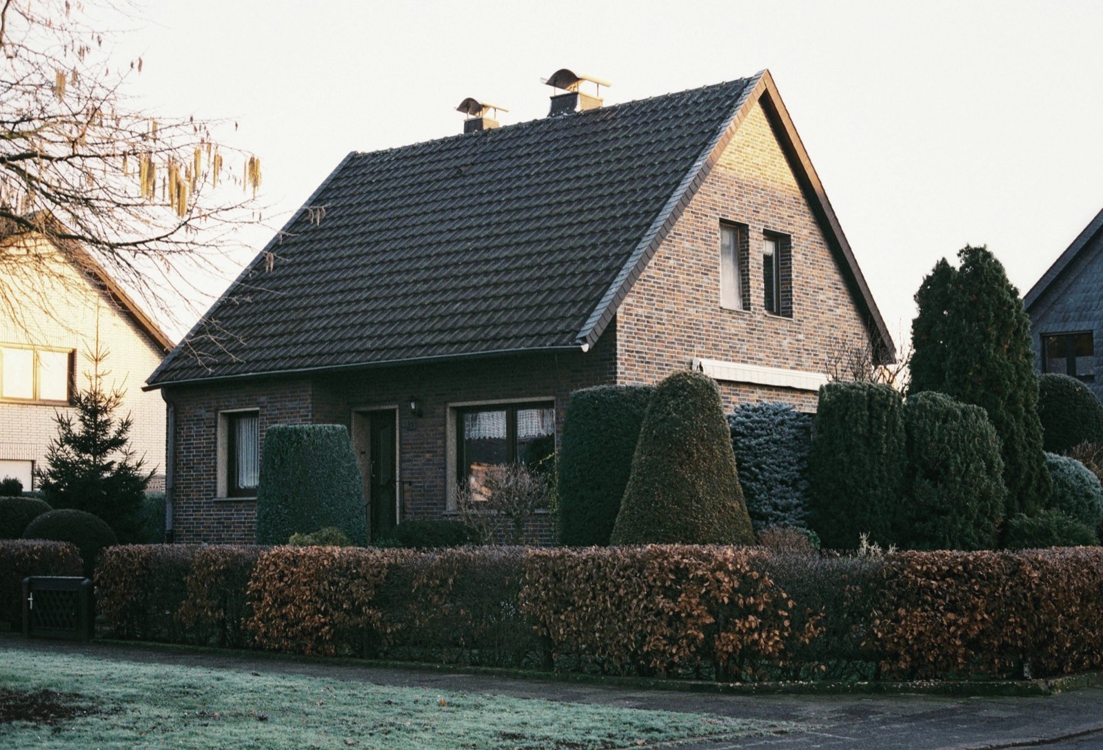 Einfamilienhaus aus rotem Backstein mit Hecke und Vorgarten im Morgenlicht